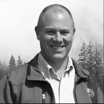 A Black and White photo of David Fitz-Gerald, a balding white man standing outside with a button up shirt and an outdoor jacket