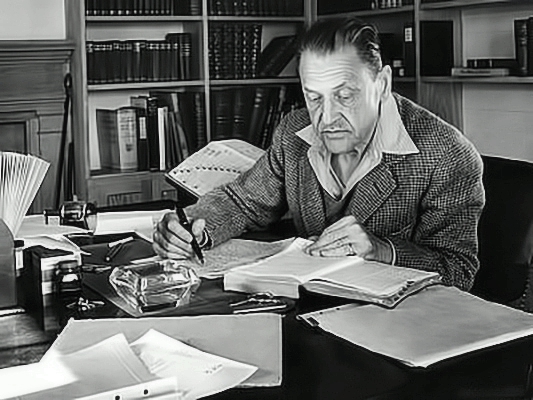W. Somerset Maugham sitting at his desk pouring over journals
