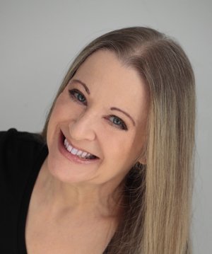 A white woman with blue eyes and blonde hair smiling against a gray backdrop